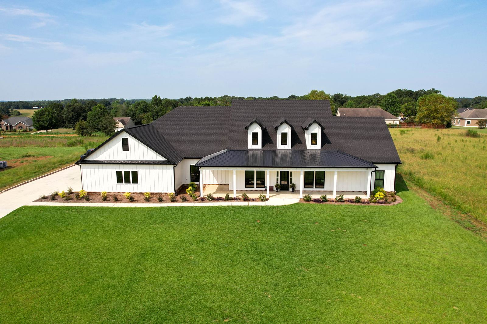 Modern white farmhouse with a wraparound porch and black metal roof, photographed for a Wiregrass real estate listing